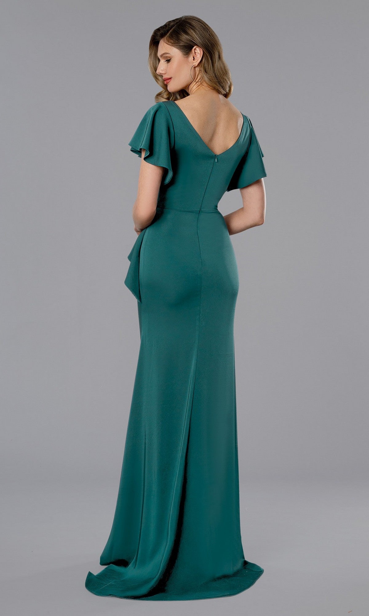 Woman modeling the Stella Couture 25352 long formal dress in teal, featuring flutter sleeves, a fitted waist, and a V-shaped back, posed against a plain grey background.
